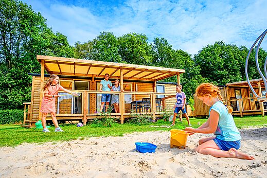 Familie speelt voor een houten stacaravan op camping CAPFUN Eibernest in Eibergen.