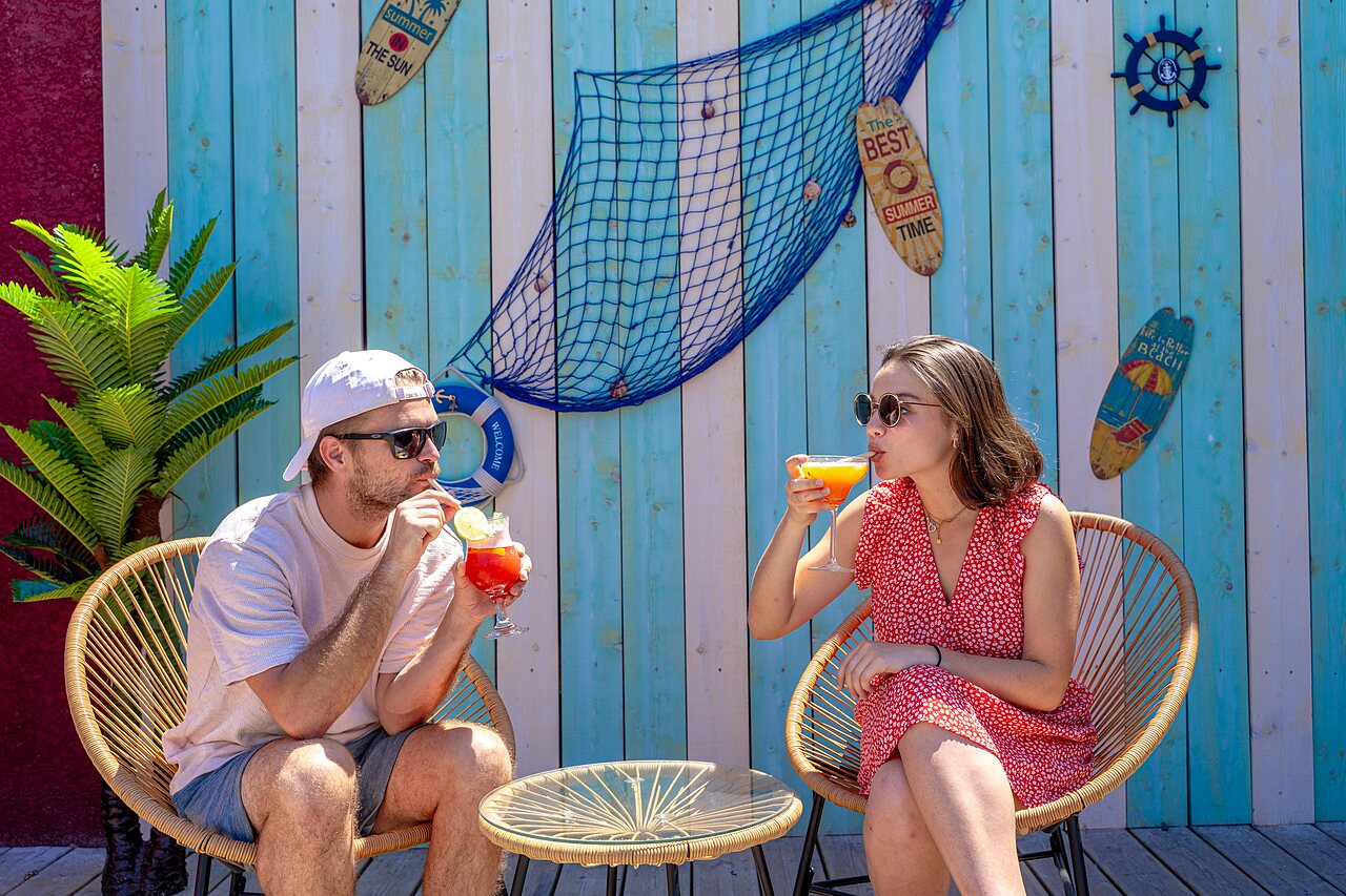 Koppel geniet van cocktails aan de gedecoreerde buitenbar op camping VAGUES OCEANES Elys�e in Le Grau du Roi (30).