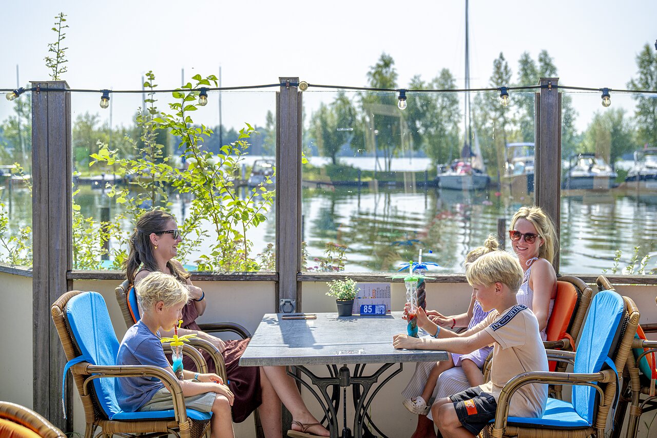 Familie aan de bar, verfrissende drankjes, uitzicht op het meer op camping CAPFUN Erkemederstrand in Zeewolde.