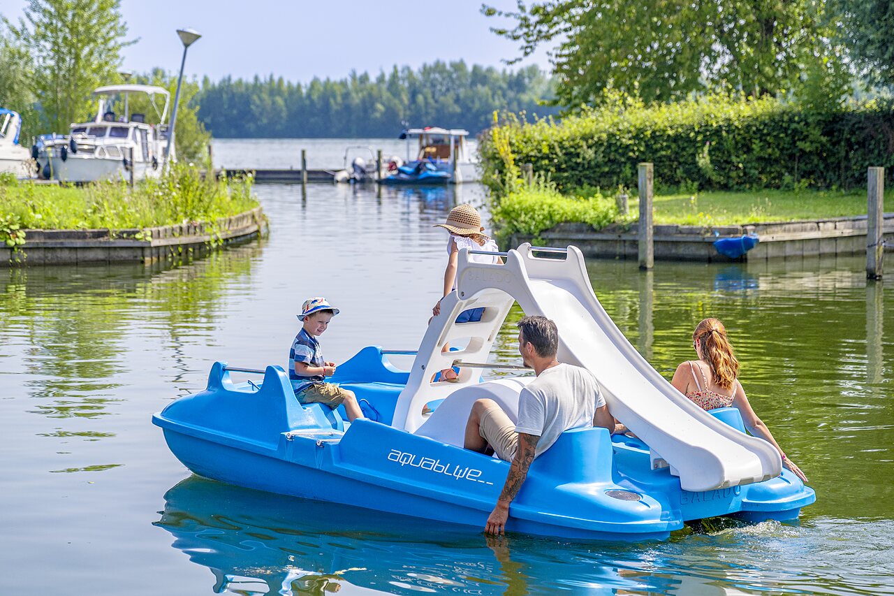 Familie op waterfiets met glijbaan bij camping CAPFUN Erkemederstrand in Zeewolde.