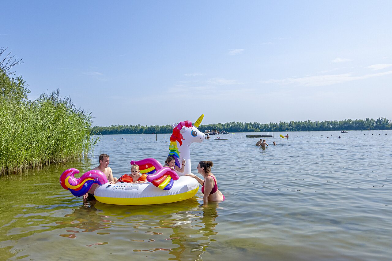 Familie speelt in het meer met opblaasbare eenhoorn op camping CAPFUN Erkemederstrand in Zeewolde.