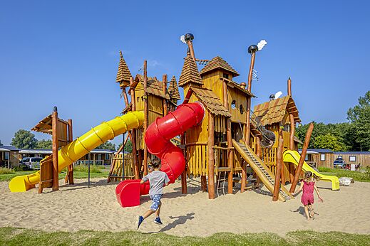 Houten speeltuin met glijbanen en kinderen op camping CAPFUN Erkemederstrand in Zeewolde.