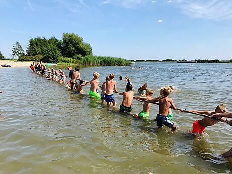 Kinderen touwtrekken in het water op camping CAPFUN Erkemederstrand in Zeewolde.