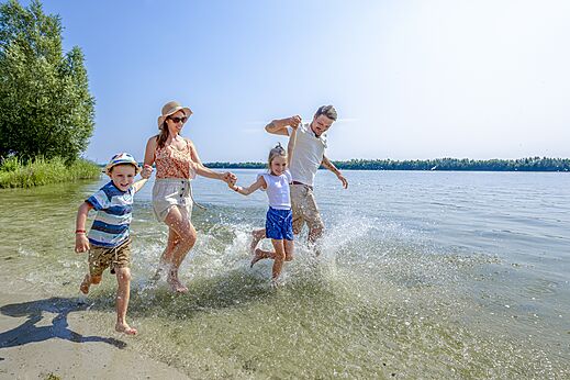 Vrolijke familie rent en spettert op strand bij camping CAPFUN Erkemederstrand in Zeewolde.