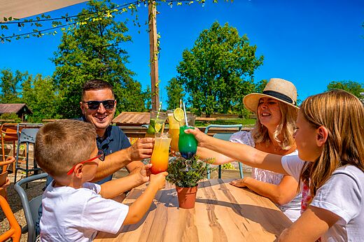 Lachende familie proost met kleurrijke cocktails aan de bar van camping CLICOCHIC Etang de la Mutche in HARPRICH (57).