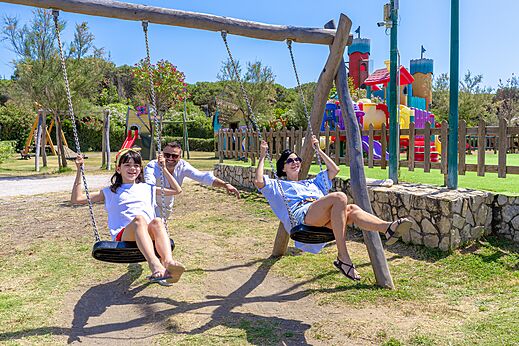 Lachende familie op de schommels van de speeltuin op camping CAPFUN Europing in Tarquinia (01).