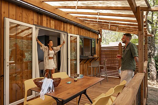 Modern stacaravan met groot houten terras en lachend stel op camping CLICOCHIC Eyrieux in Les OLLIERES-SUR-EYRIEUX.