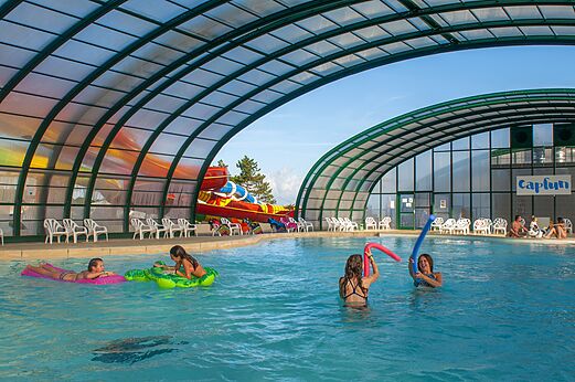 Overdekt zwembad, glijbaan en kinderen op camping CAPFUN Falaises in Gonneville sur Mer.