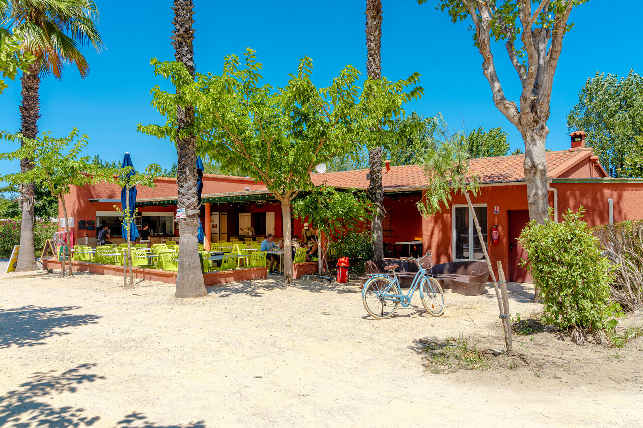 Buitenterras van restaurant-bar met palmbomen op camping VAGUES OCEANES Au Flamenco Argel�s-sur-Mer.