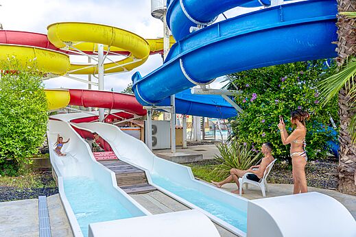 Kleurrijke waterglijbanen en kind dat glijdt op camping CAPFUN Fleurs d'Agde in AGDE (34).