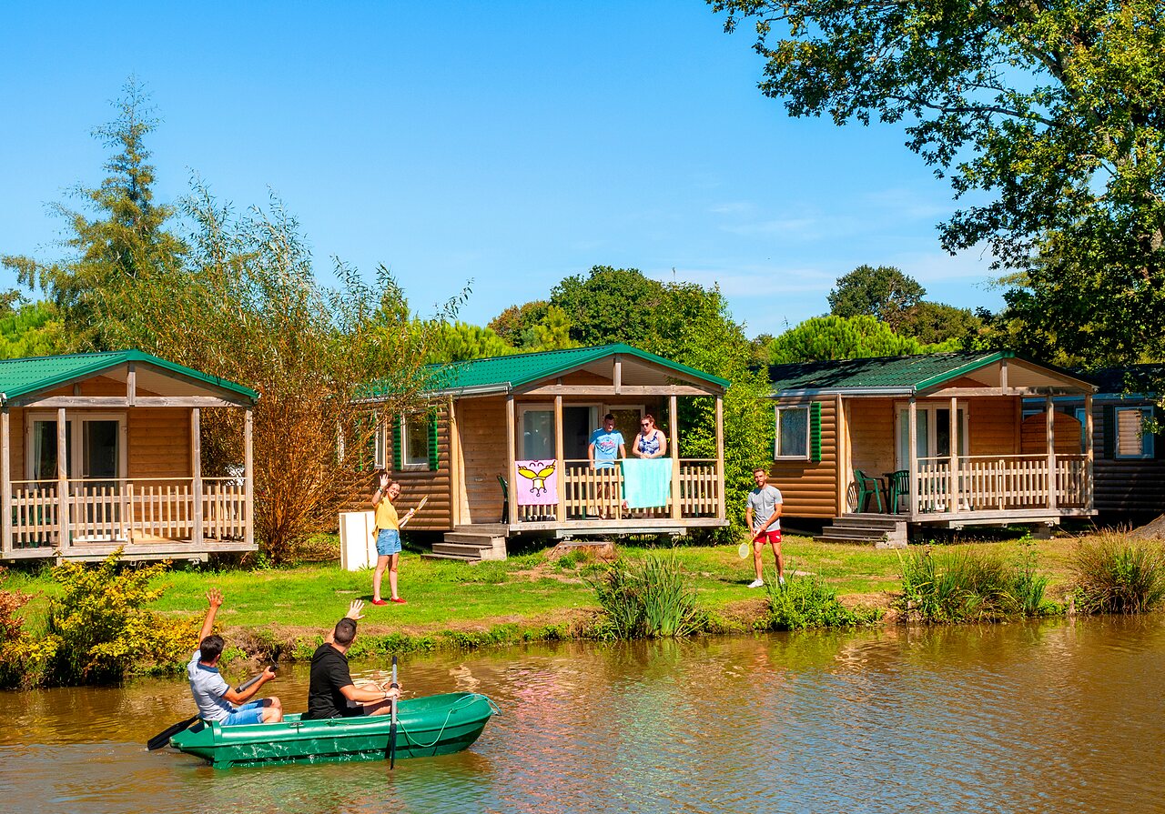 Houten chalets aan een vijver met wateractiviteiten op camping CAPFUN Forges in Avrille (85).