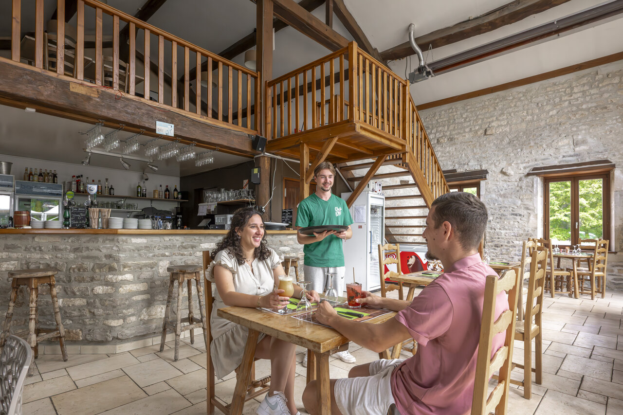 Restaurant-bar interieur, stel en ober op camping CLICOCHIC Forge Sainte Marie Thonnance-les-Moulins.