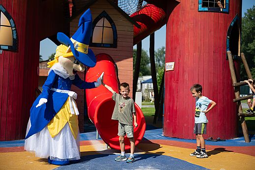 Mascotte en kinderen spelen bij een glijbaan op camping CAPFUN Fort Bedmar in Sint-Gillis-Waas.