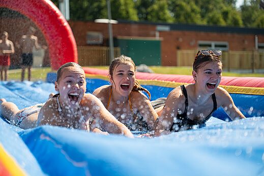Jonge vrouwen plezier op opblaasbare waterglijbaan op camping CAPFUN Fort Bedmar in Sint-Gillis-Waas.