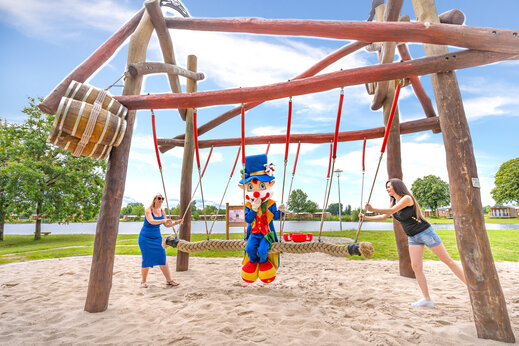 Speeltuin met houten schommel en mascotte op camping CAPFUN Fort Falabraque in Seltz.