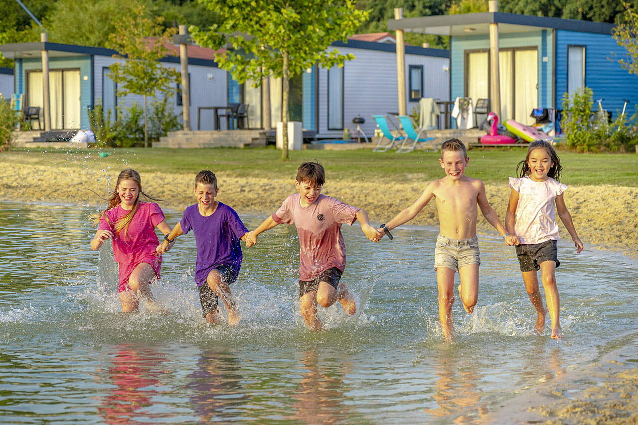 Vrolijke kinderen rennen in ondiep water voor stacaravans op camping CAPFUN De Fruithof in Klijndijk.