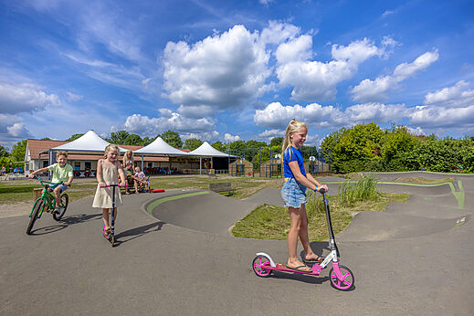 Kinderen spelen op de pumptrack met scooters en fiets op camping CAPFUN De Fruithof in Klijndijk.