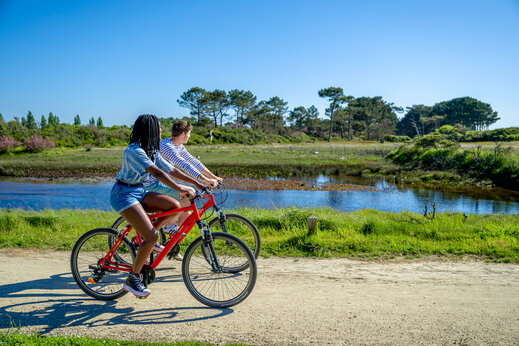 Twee personen fietsen op zandpad langs water, op camping CAPFUN Grand Large in FOUESNANT (29).