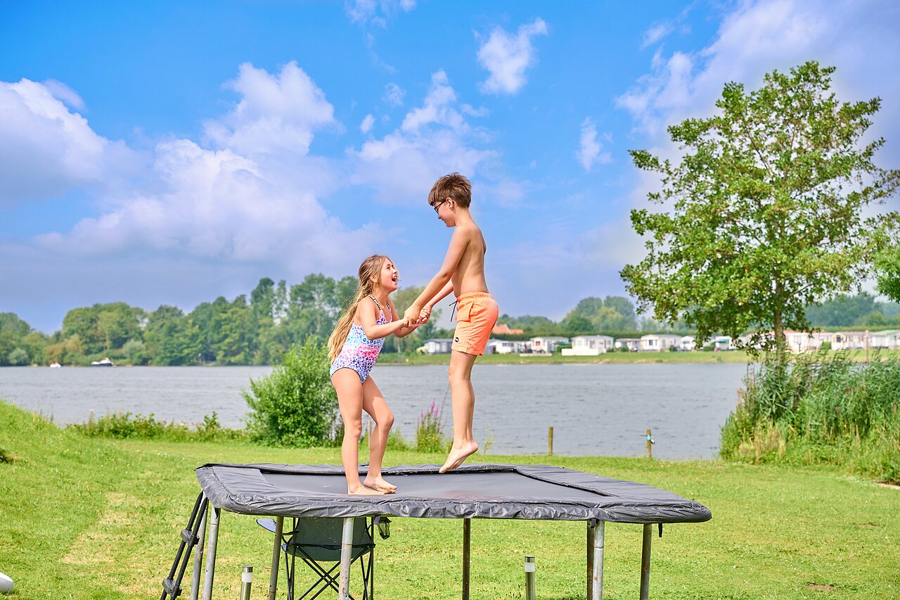 Twee kinderen springen op buitentrampoline bij het meer op camping CAPFUN Groene Eiland in Appeltern.