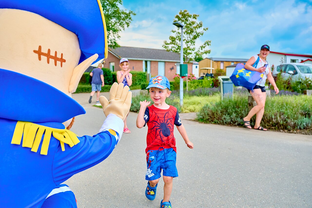 Mascotte zwaait naar lachend kind tijdens animatie op camping CAPFUN Groene Eiland in Appeltern.