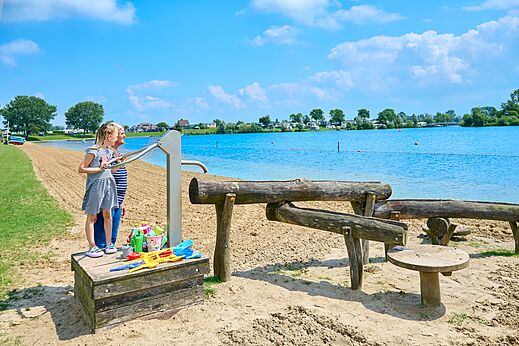 Zandstrand met waterspeeltoestellen en kinderen op camping CAPFUN Groene Eiland in Appeltern.