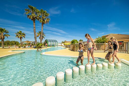 Lagunezwembad met waterspellen en palmbomen op camping VAGUES OCEANES Hamacs in Fleury (11).