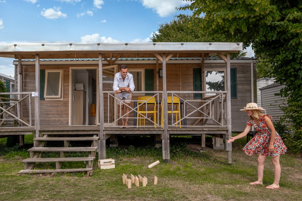 Houten stacaravan met terras, stel speelt M�lkky op camping CLICOCHIC Haras de Deauville in Touques.