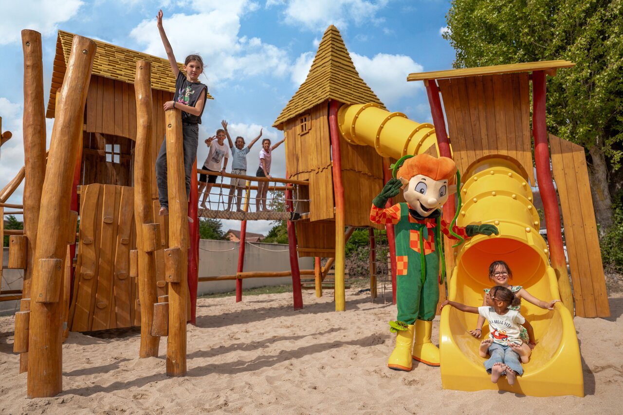 Houten speeltuin, glijbanen, kinderen en mascotte op camping CLICOCHIC Haras de Deauville.