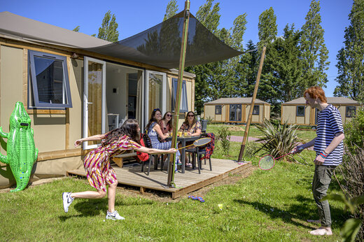 Modern Mobil-home met terras, familie speelt badminton op camping CAPFUN Hautes Coutures.