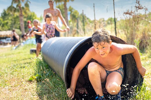Kind komt uit een watertunnel, spel op camping CAPFUN Hauts de Ratebout in STE FOY DE BELVES (24).