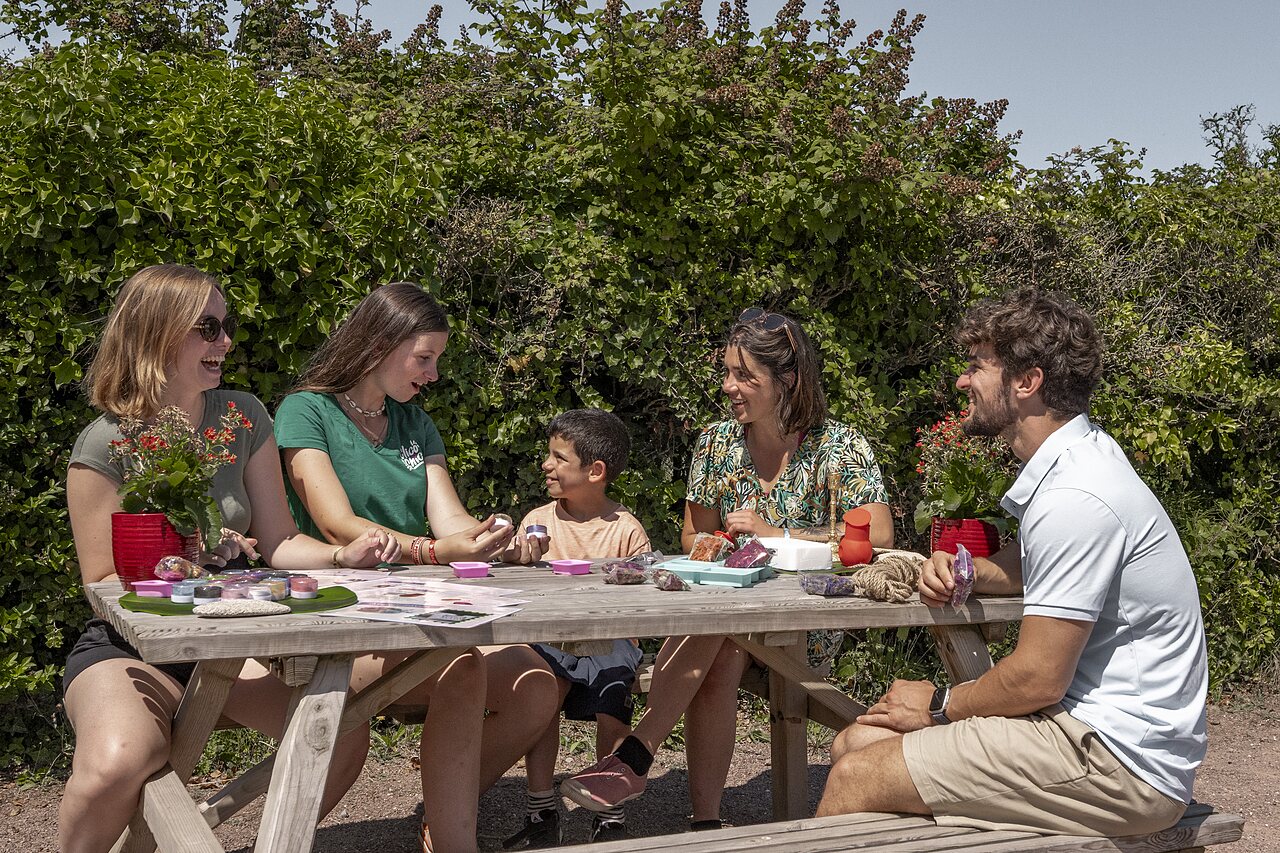 Familie neemt deel aan creatieve workshop buiten op camping CLICOCHIC Havre de Berni�res.