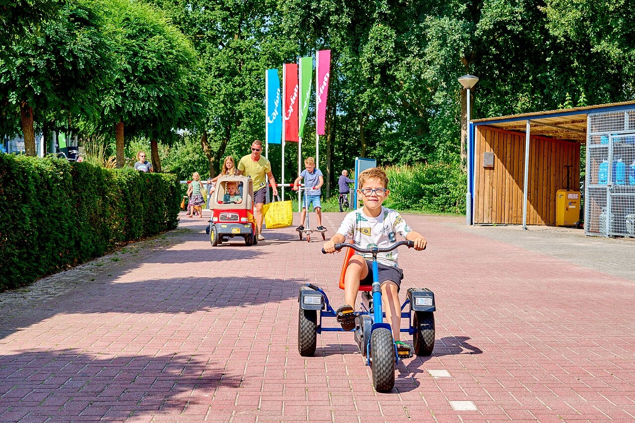 Kinderen spelen met skelter, step en speelgoedauto op camping CAPFUN Heino in Heino.