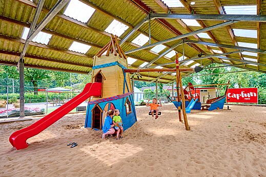 Overdekte speeltuin met glijbanen en schommels voor kinderen op camping CAPFUN Heino in Heino.