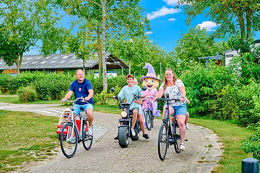 Familie op de fiets met mascotte en diverse voertuigen op camping CAPFUN Heino in Heino.