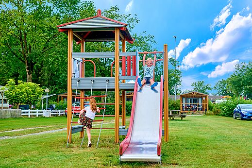 Speeltuin met glijbaan en spelende kinderen op camping CAPFUN Heino in Heino.