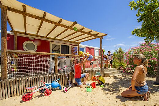 Rode Mobil-home met terras, familie en spelende kinderen op camping CAPFUN Hermitage in SERIGNAN (34).