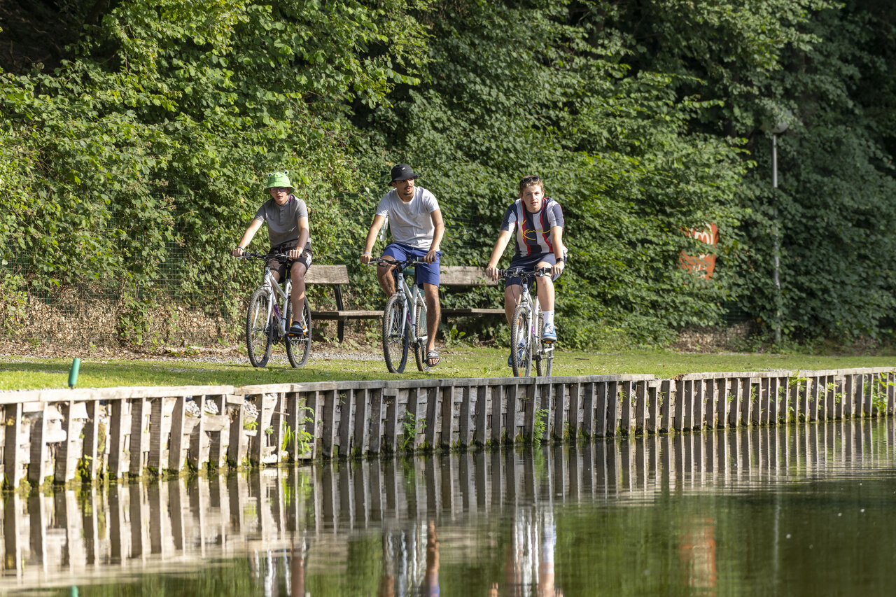 Drie jonge mannen fietsen langs een vijver, natuur, op camping CAPFUN Hirondelle in Oteppe.
