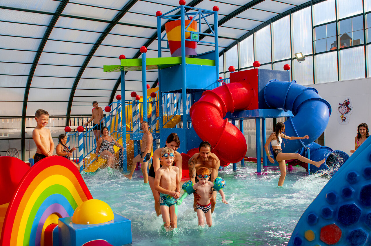 Overdekt waterpark met kleurrijke glijbanen en waterspelen op camping CAPFUN Hirondelle in Oteppe.