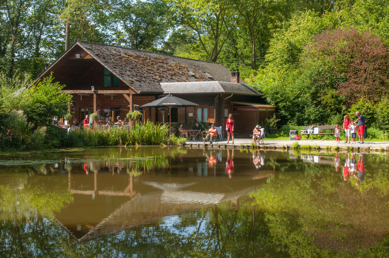 Restaurantgebouw met terras aan de vijver, vissers op camping CAPFUN Hirondelle in Oteppe.