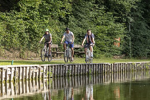 Drie personen fietsen langs een waterloop op camping CAPFUN Hirondelle in Oteppe.