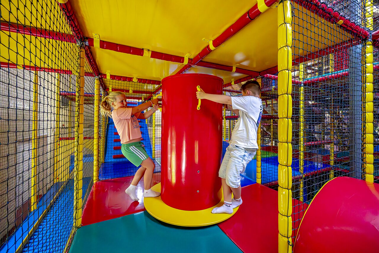 Kinderen spelen in een kleurrijke indoor speelstructuur op camping CAPFUN IJsselstrand in Doesburg.