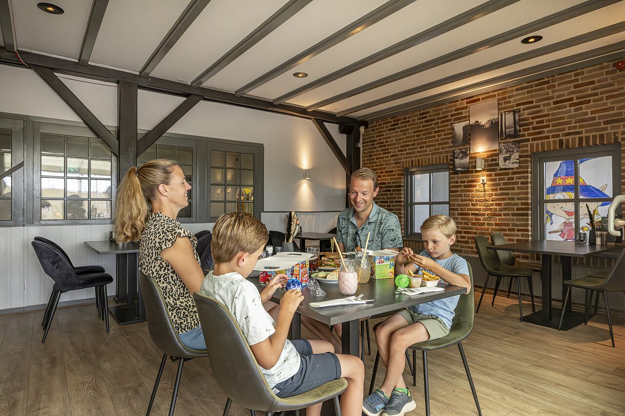 Familierestaurant met spelende kinderen aan tafel op camping CAPFUN IJsselstrand in Doesburg.