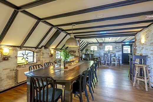 Restaurant en bar met lange houten tafel en bakstenen muren op camping CAPFUN IJsselstrand in Doesburg.