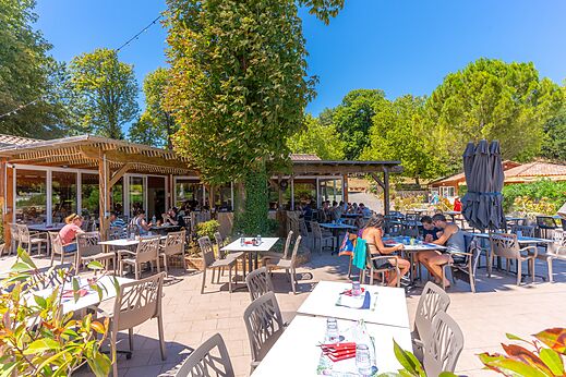 Zonnig terras van het restaurant met gasten op camping CAPFUN Imbours in LARNAS (07).