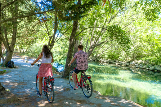 Koppel fietst langs schaduwrijke rivier op camping CAPFUN Jantou in LE THOR (84).