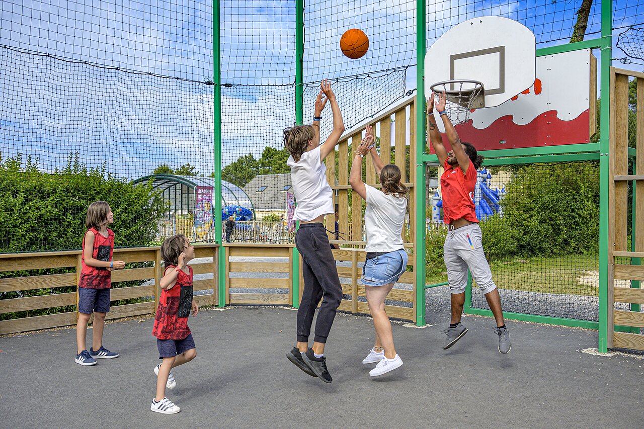 Familie en animator spelen basketbal op multisportterrein bij CAPFUN Joncal.