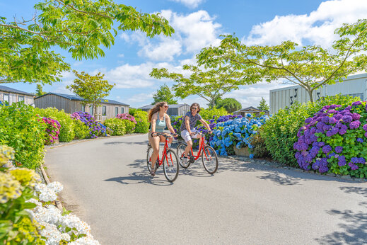 Twee personen fietsen op bloemrijke laan op camping CAPFUN Kervel in PLONEVEZ PORZAY (29).