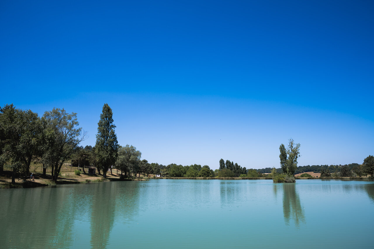 Groot rustig meer omringd door groene bomen op camping CAPFUN Lac des 3 Vall�es in Lectoure (32).