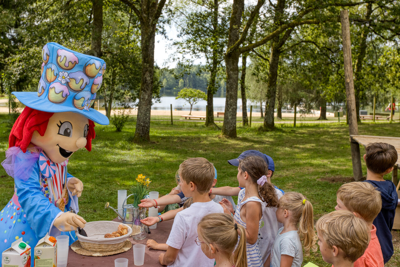Mascotte leidt kinder snacktijd aan het meer, camping CLICOCHIC Lac de Miel.