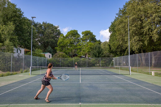 Buiten tennisbaan met spelers op camping CLICOCHIC Lac de Miel, Beynat.